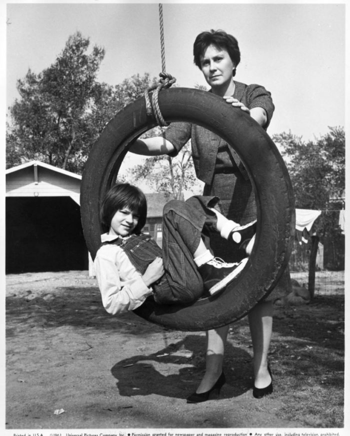 Book author Harper Lee (standing) and Mary Badham (in the tire swing), who plays Scout in the film version of "To Kill a Mockingbird," are shown on a film set at Universal Studio. 1961 file photo courtesy of Universal Pictures.
